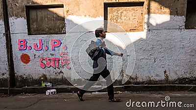 An Indian man walking past a grungy wall painted with political campaign of the Editorial Stock Photo