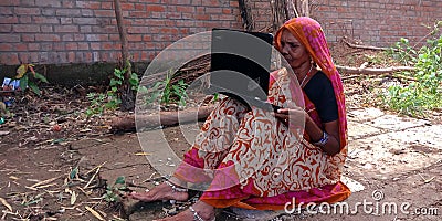 An Indian matured women using laptop seating at farmers field Editorial Stock Photo