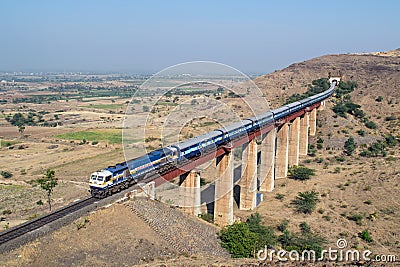 Indian railways long passenger train, exiting a tunnel to cross a tall railway bridge Stock Photo