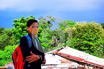 Indian rural school student wears uniform and wears face mask for coronavirus safety protection. with background of greenery and Stock Photo