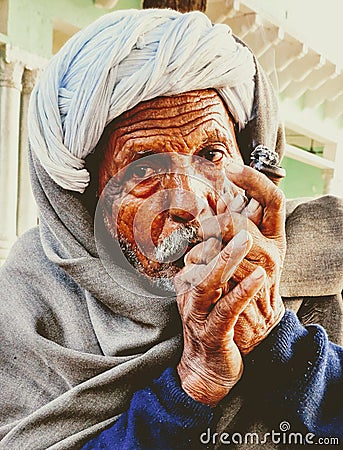 Indian village old man smoking Ganja Marihuana with chillum/hukkah in Rajasthan's traditional dress turban on head in winter Editorial Stock Photo