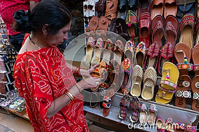 Indian woman checking pairs of Rajasthani womens` shoes at display for sale. Editorial Stock Photo