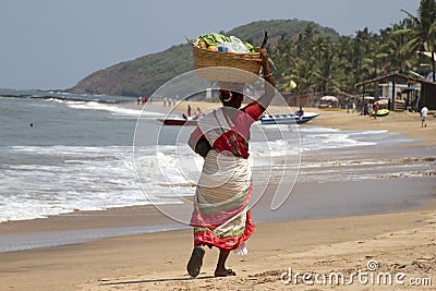 The Indian woman in a sari bears fruit on the head on a beach. India Goa Editorial Stock Photo