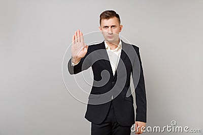 Indifferent young business man in classic black suit, shirt showing stop gesture with palm isolated on grey wall Stock Photo