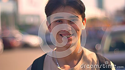 Indivíduo asiático feliz que riem da câmera, close-up que estão na rua, carros e estrada no fundo, vida urbana vídeos de arquivo Indivíduo asiático feliz que riem da câmera, close-up que estão na rua, carros e estrada no fundo, vida urbana vídeos de arquivo