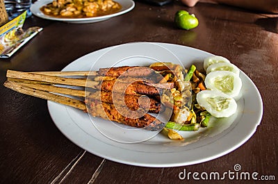 Indonesian dish Lombok: Sate Pusut marinated meat mix on stick on table with other dishes in background Stock Photo