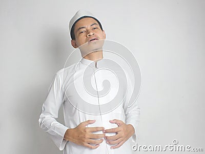 Indonesian Muslim men wear gray skullcap and white robe touch his stomach satiated eating too much break the fast. Full. Stuffed Stock Photo