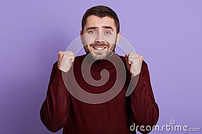 Indoor portrait of emotional charismatic good looking man with beard clenching fists, making gesture, smiling sincerely, having Stock Photo