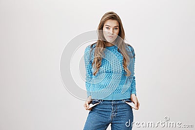 Indoor portrait of sad and gloomy cute caucasian female showing empty pockets while standing over gray background. Woman Stock Photo