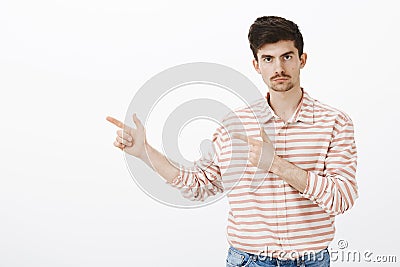 Indoor portrait of serious jealous boyfriend with beard and moustache, pointing left with finger gun gestures and Stock Photo