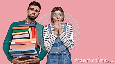 Indoor shot of displeased surprised young woman and man, hold textbooks, stand closely to each other, reads scientific Stock Photo