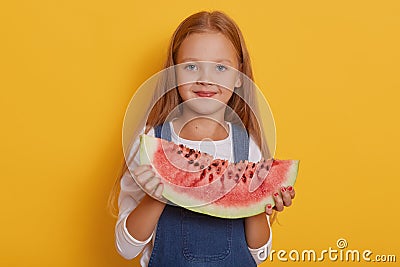 Indoor shot of little charming girl with portion of sweet watermelon in her hands, charming blonde modelposing over Stock Photo