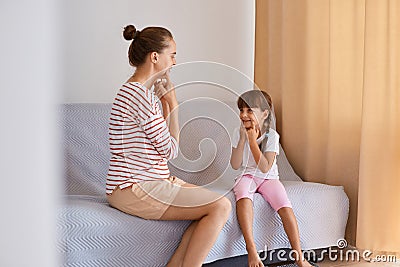 Indoor shot of pleasant looking woman speech pathologist having lesson with little girl, people sitting on comfortable sofa near Stock Photo