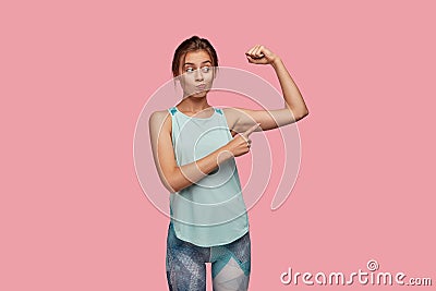 Indoor shot of puzzled young woman purses lips in discontent, raises right hand and indicates at biceps, being Stock Photo