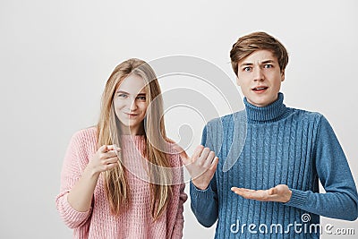 Indoor shot of shocked male and frowning female wearing colourful sweaters looking at camera. Boy pointing with fingers Stock Photo