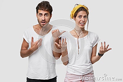 Indoor shot of stupefied indignant young man points at his wife, look troublesome at camera, have puzzled facial Stock Photo