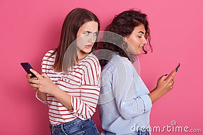 Indoor shot of women looking at mobile phone and seeing bad news message or photos while standing back to back to each other. Stock Photo