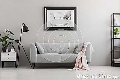Industrial black floor lamp and a pink blanket on an elegant settee with cushions in a gray living room interior with place for a Stock Photo