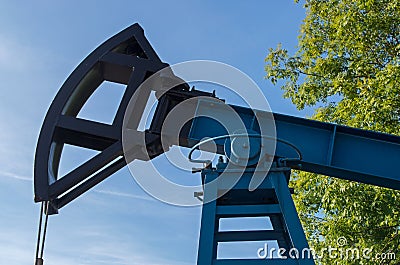 Industrial block pumping unit with blue painted body, black rocking element with rope against blue sky and greenery Stock Photo