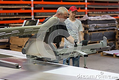 Industrial carpenter worker operating wood cutting machine during wooden door furniture manufacturing Editorial Stock Photo