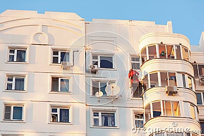 Industrial climber fixed on safety ropes puttying and painting facade of building on sunny day. Bottom view from afar Stock Photo