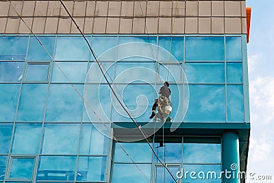 Industrial climber hanging on the clothesline and washes Windows, glass facade modern building Editorial Stock Photo