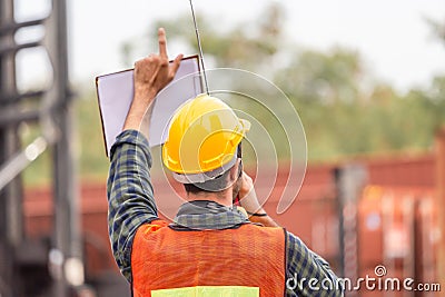 Industrial engineer in hard hat containers box background, Dock worker man talks on two-way radio with holding clipboard checklist Stock Photo