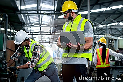 Industrial engineer wearing helmet and safe glasses, holding laptop computer for operating machinery at manufacturing plant Stock Photo