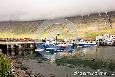 The industrial harbour of the Isafjordur in Iceland with a yachts, blue boat IS141 and mountain covered in misty clouds Editorial Stock Photo