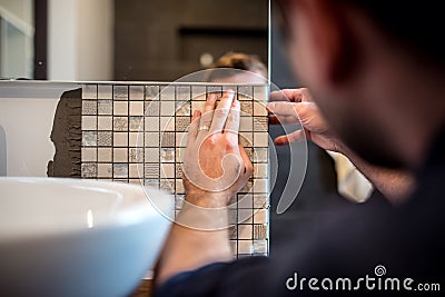 Industrial man worker applying mosaic tiles in bathroom walls Stock Photo