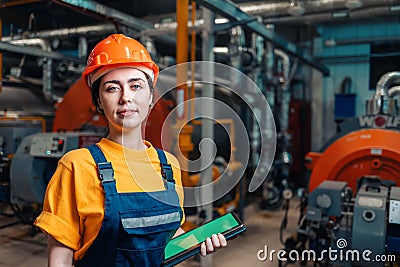 Industrial production concept. Portrait of a female engineer in uniform and helmet with a tablet in her hand. In the background- Stock Photo