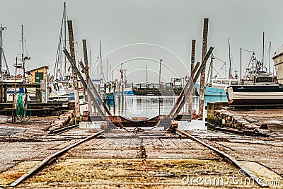 An industrial rail boat ramp or boat deployer on platform in a fishermen village is rusty and seems misused and abandoned. Dragor Stock Photo