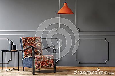 An industrial side table and a boho armchair in an elegant, gray living room interior with molding and place for a coffe table. Re Stock Photo