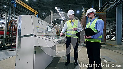 Industrieel bedieningspaneel en twee ingenieurs die in de buurt van het panel in een moderne fabrieksvloer praten stock videobeelden Industrieel bedieningspaneel en twee ingenieurs die in de buurt van het panel in een moderne fabrieksvloer praten stock videobeelden