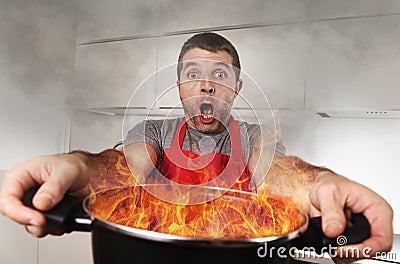 Inexperienced home cook with apron holding pot burning in flames with stress panic face expression Stock Photo