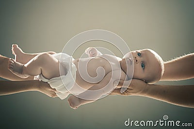 Infant held by hands of both parents on gray background. Stock Photo