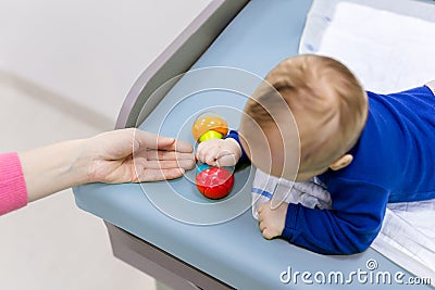 Infant with mother playing on changing table. Mom giving rattle toy to baby boy. View from above Stock Photo