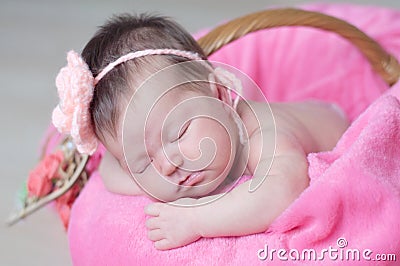 Infant sleeping in basket with knitted flower on head, baby girl lying on pink blanket, cute child, newborn Stock Photo