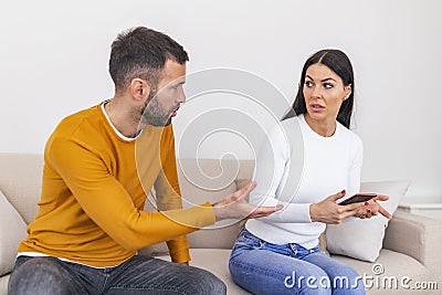 Infidelity. Jealous boyfriend Showing his Cheating girlfriend her Phone Demanding Explanation Sitting On Sofa Indoor. Wife caught Stock Photo