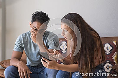 Infidelity. Jealous girlfriend Showing his Cheating boyfriend his Phone Demanding Explanation Sitting On Sofa Indoor at home. Wife Stock Photo