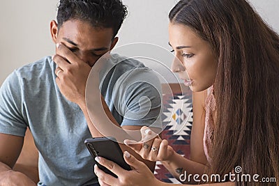 Infidelity. Jealous girlfriend Showing his Cheating boyfriend his Phone Demanding Explanation Sitting On Sofa Indoor at home. Wife Stock Photo