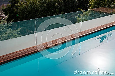 Infinity swimming pool with glassy safe fence and hardwood decking edge overlooking nature Stock Photo