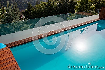 Infinity swimming pool with glassy safe fence and hardwood decking overlooking landscape Stock Photo