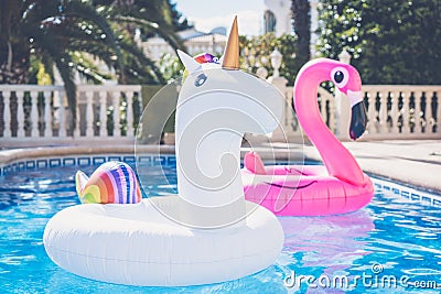 Inflatable colorful white unicorn and pink flamingo at the swim pool. Vacation time in the swimming pool with plastic Stock Photo