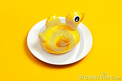 Inflatable mini yellow chicken or duckling on white plate on yellow background. Creative food concept tobacco chicken. Flat lay Stock Photo