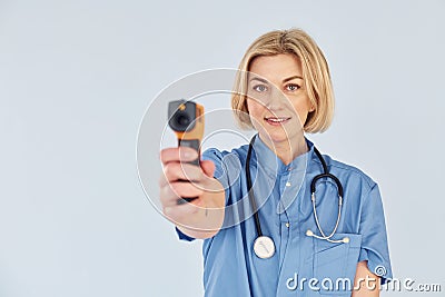 With infrared thermometer. Middle-aged professional female doctor in uniform and with stethoscope Stock Photo