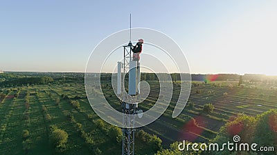 Ingenieur mit Gerät schloss eine Mobilkommunikation auf Radiotelekommunikationsturm auf Hintergrund des blauen Himmels mit an stock footage Ingenieur mit Gerät schloss eine Mobilkommunikation auf Radiotelekommunikationsturm auf Hintergrund des blauen Himmels mit an stock footage