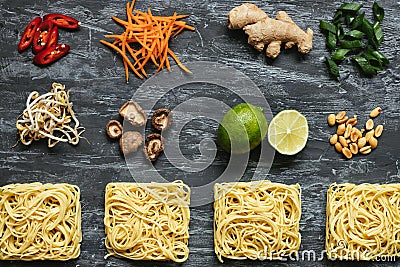 Ingredients for asian dish. Dried asian noodles with lime, nuts, cilantro and vegetables on wooden background Stock Photo