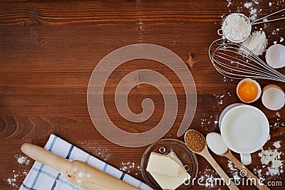 Ingredients for baking dough including flour, eggs, milk, butter, sugar, whisk and rolling pin on wooden rustic background Stock Photo