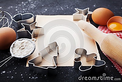 Ingredients for christmas baking. Cookies cutters, flour, rolling pin, eggs and paper sheet on kitchen black table. Stock Photo